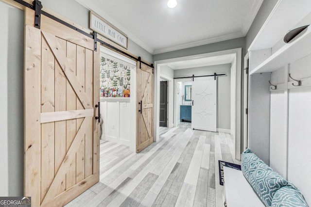 mudroom with a barn door, crown molding, baseboards, and wood finished floors