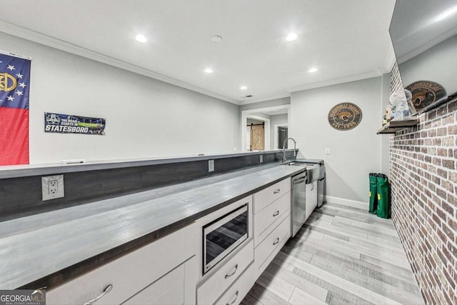 kitchen with light wood finished floors, appliances with stainless steel finishes, ornamental molding, white cabinets, and a sink