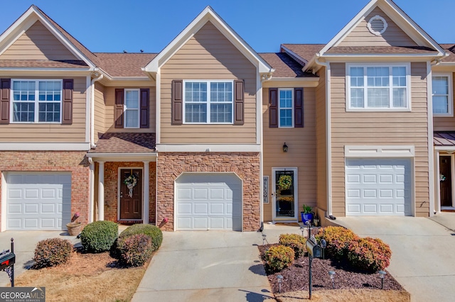 multi unit property with an attached garage, concrete driveway, roof with shingles, and stone siding