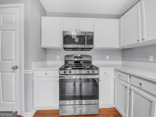 kitchen with white cabinets, light wood-style flooring, appliances with stainless steel finishes, light countertops, and a textured ceiling