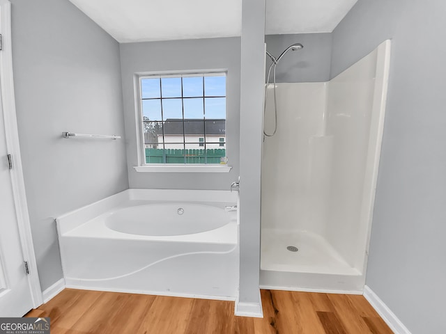 bathroom featuring a garden tub, baseboards, walk in shower, and wood finished floors