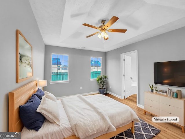 bedroom with visible vents, baseboards, a raised ceiling, light wood-style flooring, and ensuite bathroom