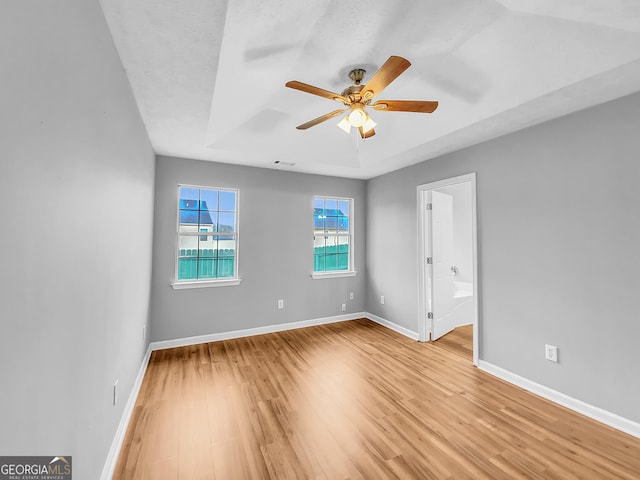 spare room with visible vents, light wood-style floors, a ceiling fan, baseboards, and a raised ceiling