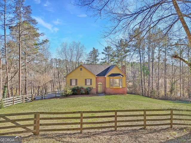 view of front of property featuring a fenced front yard, brick siding, a front lawn, a chimney, and a view of trees