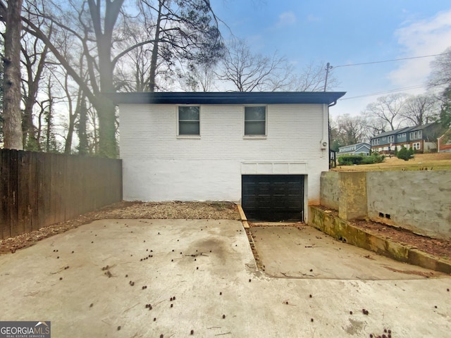 view of home's exterior featuring a garage, concrete driveway, brick siding, and fence