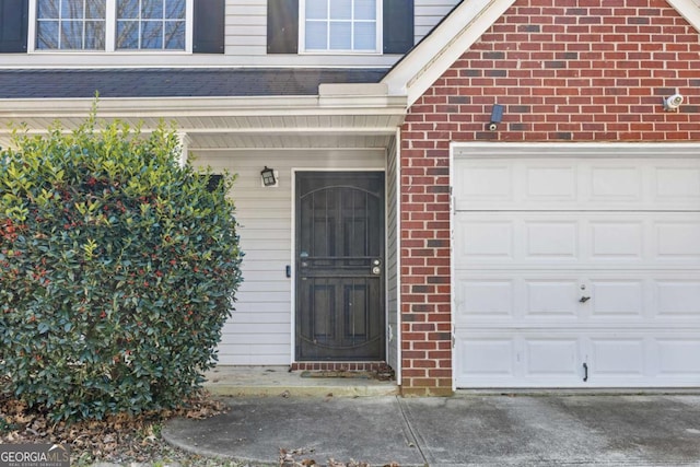 view of exterior entry featuring an attached garage and brick siding