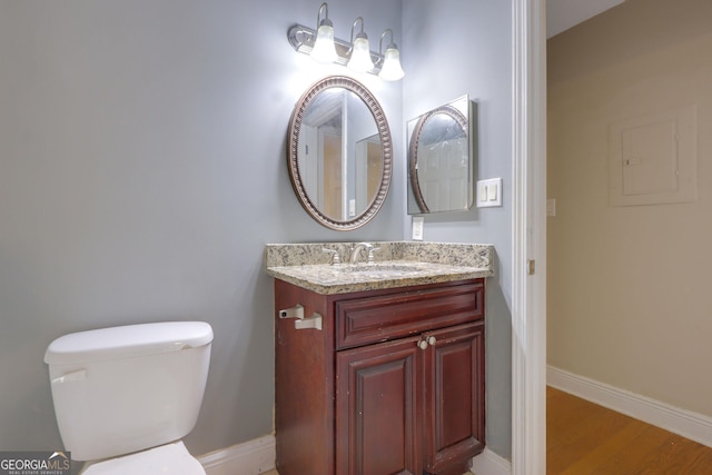 bathroom with vanity, toilet, wood finished floors, and baseboards