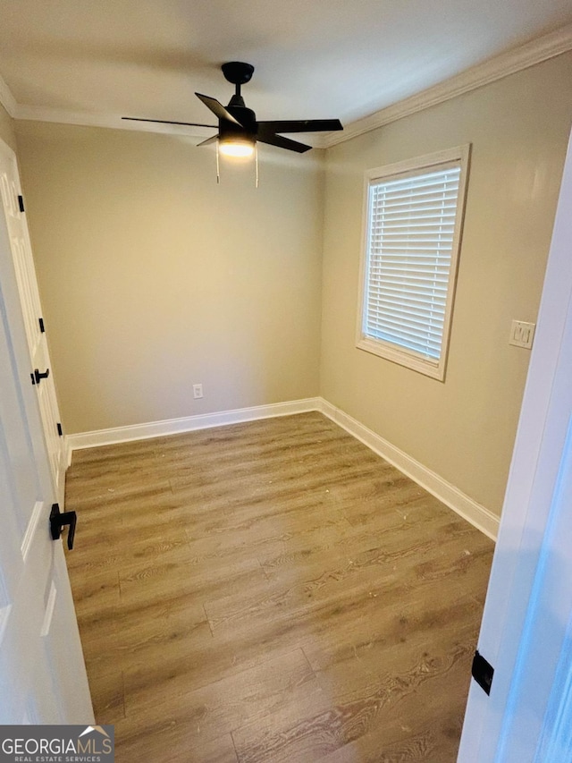 empty room with ceiling fan, crown molding, baseboards, and wood finished floors