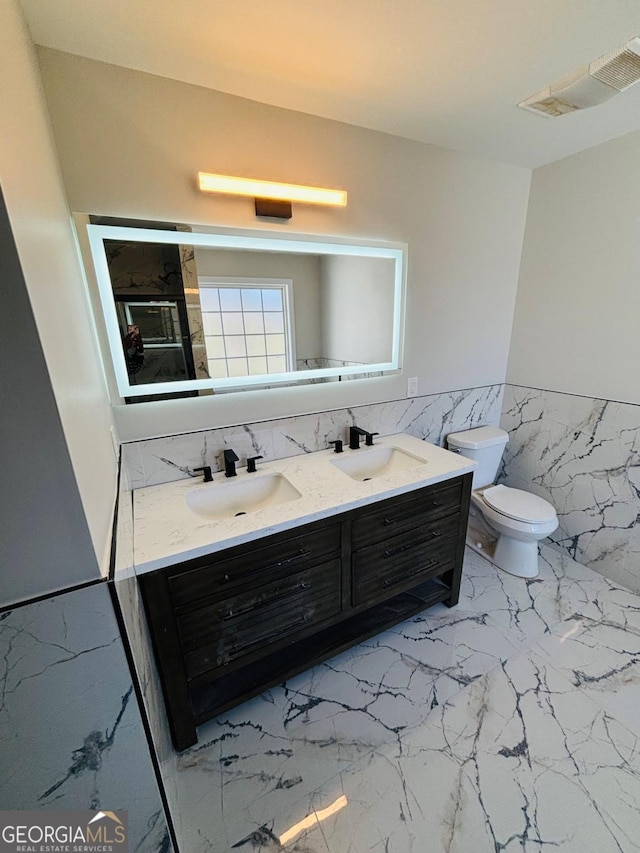 full bath with double vanity, marble finish floor, toilet, and a sink