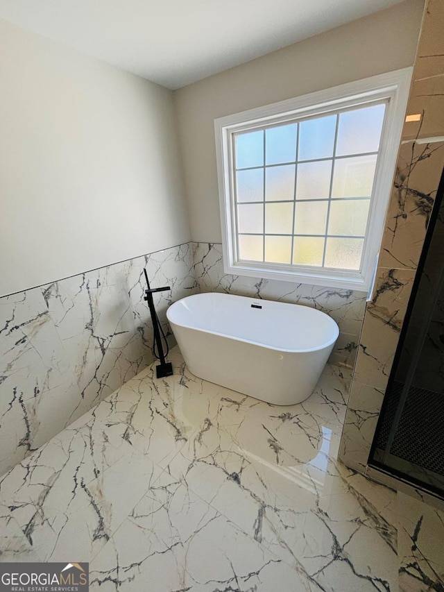 bathroom with marble finish floor, tile walls, a freestanding bath, a stall shower, and wainscoting