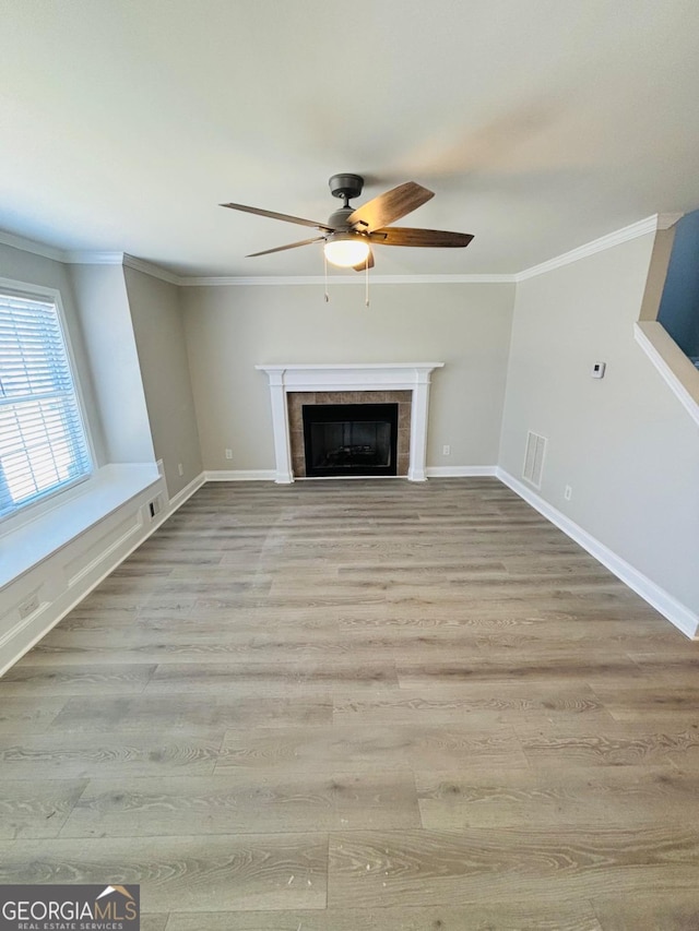 unfurnished living room featuring light wood-style flooring, ornamental molding, baseboards, and a tile fireplace