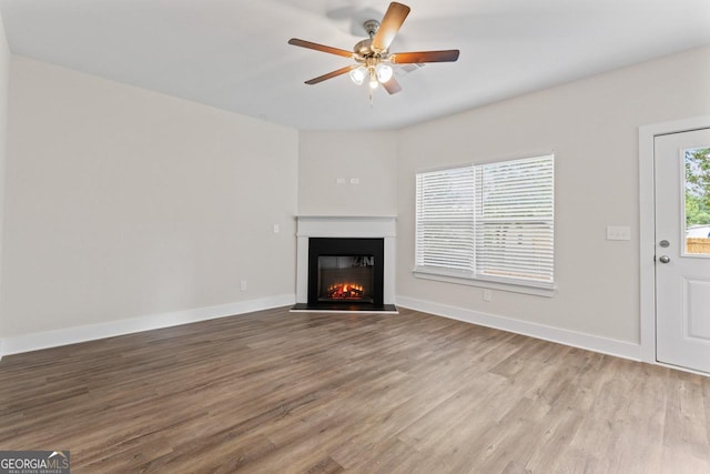 unfurnished living room with baseboards, a ceiling fan, a glass covered fireplace, and wood finished floors