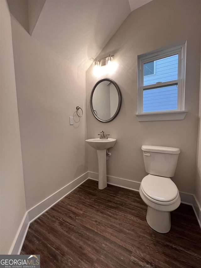 half bath with lofted ceiling, wood finished floors, toilet, and baseboards