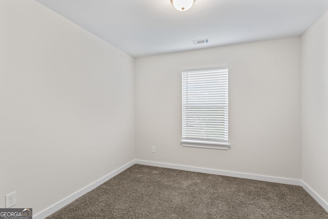empty room featuring baseboards, visible vents, and dark carpet