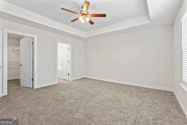 unfurnished bedroom featuring baseboards, a raised ceiling, carpet, and a spacious closet