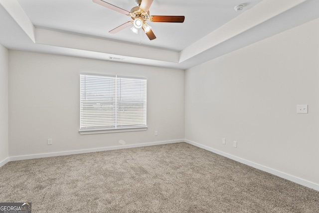 empty room featuring a ceiling fan, visible vents, baseboards, a raised ceiling, and carpet flooring
