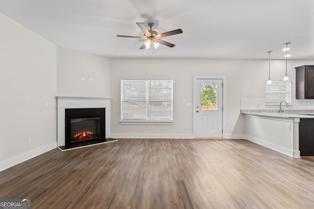unfurnished living room featuring baseboards, a ceiling fan, a glass covered fireplace, and wood finished floors