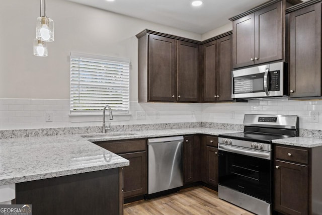 kitchen with dark brown cabinets, appliances with stainless steel finishes, a sink, light wood-style flooring, and backsplash