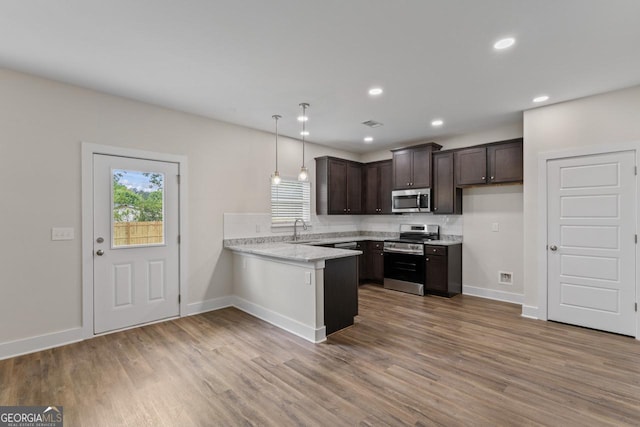kitchen with a peninsula, wood finished floors, dark brown cabinets, baseboards, and appliances with stainless steel finishes