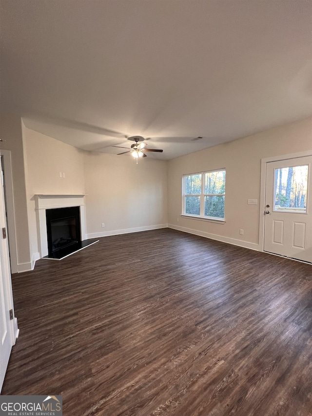 unfurnished living room featuring a fireplace with raised hearth, dark wood finished floors, baseboards, and ceiling fan