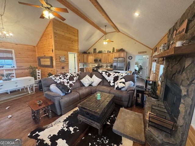 living area with ceiling fan with notable chandelier, beam ceiling, wooden walls, and wood finished floors