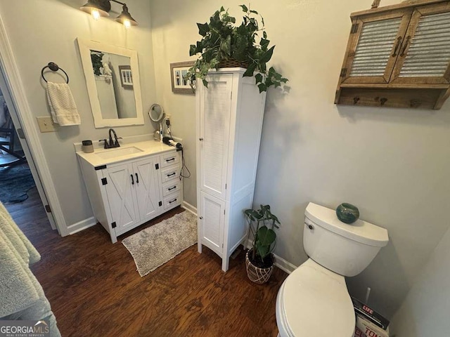 bathroom with toilet, baseboards, wood finished floors, and vanity