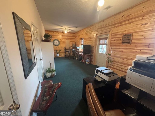 carpeted office space with visible vents, ceiling fan, wooden walls, and a textured ceiling