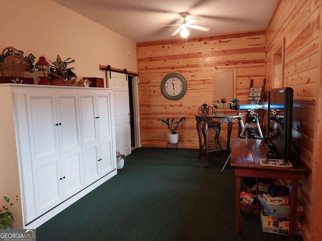 office area with a textured ceiling, a barn door, wood walls, and a ceiling fan