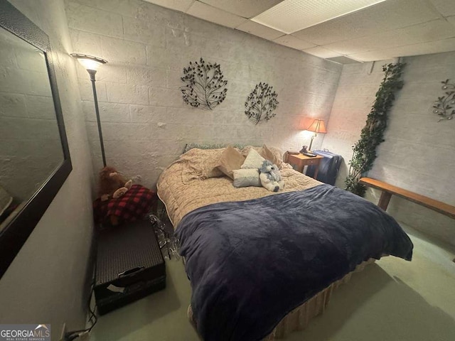 bedroom with a paneled ceiling, concrete floors, and concrete block wall