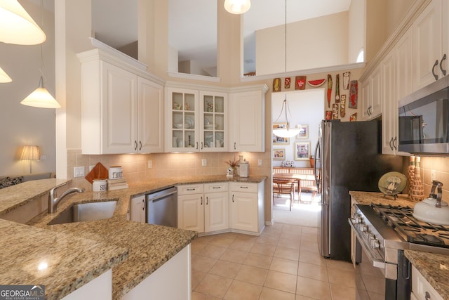 kitchen with a towering ceiling, white cabinetry, stainless steel appliances, and a sink