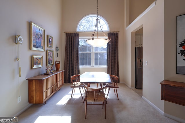 dining area with light carpet, a towering ceiling, and baseboards