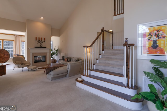 stairs with carpet floors, a glass covered fireplace, and high vaulted ceiling