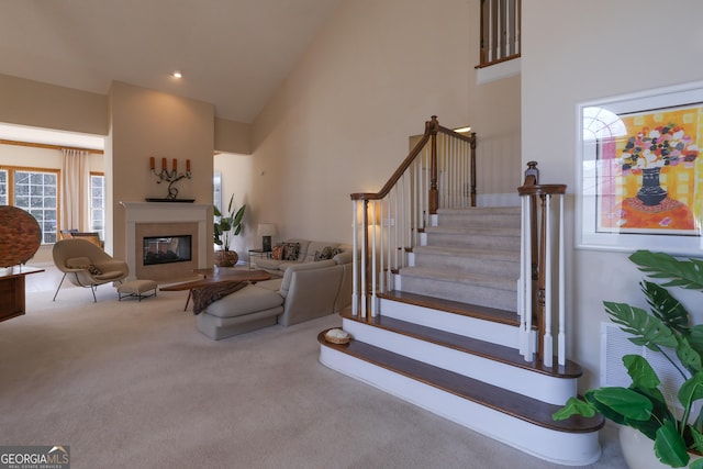 carpeted living area featuring stairway, recessed lighting, high vaulted ceiling, and a glass covered fireplace