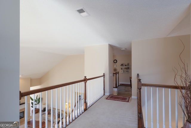 hallway featuring an upstairs landing, visible vents, vaulted ceiling, baseboards, and carpet