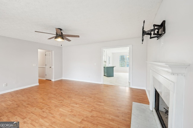 unfurnished living room featuring a textured ceiling, a ceiling fan, light wood finished floors, and a premium fireplace