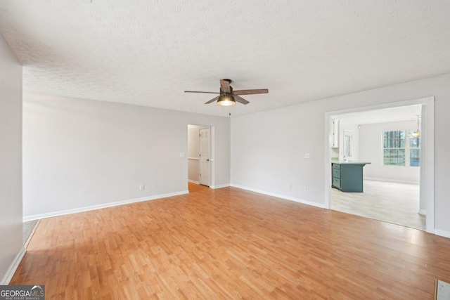 unfurnished room with ceiling fan with notable chandelier, a textured ceiling, light wood-type flooring, and baseboards