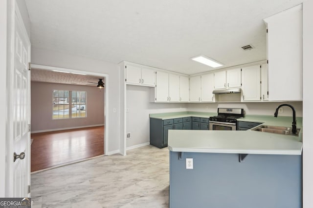 kitchen with under cabinet range hood, a sink, gas stove, a peninsula, and white cabinets