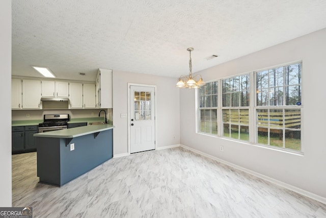 kitchen with stainless steel range with gas cooktop, under cabinet range hood, a peninsula, an inviting chandelier, and a sink