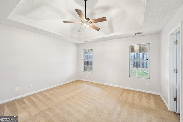 spare room featuring visible vents, baseboards, light colored carpet, a raised ceiling, and a ceiling fan