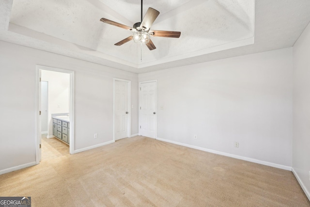 unfurnished bedroom with a raised ceiling, connected bathroom, baseboards, and light carpet