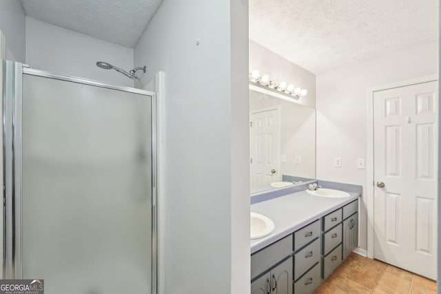 bathroom with a textured ceiling, a shower stall, double vanity, and a sink