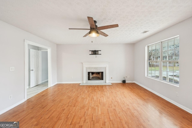 unfurnished living room featuring visible vents, light wood-style flooring, a textured ceiling, a fireplace, and baseboards