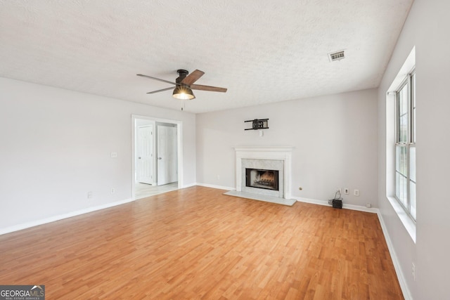 unfurnished living room with a wealth of natural light, a premium fireplace, light wood-type flooring, and a textured ceiling