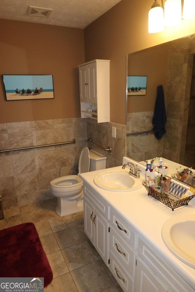 full bathroom with a textured ceiling, a sink, visible vents, and tile walls