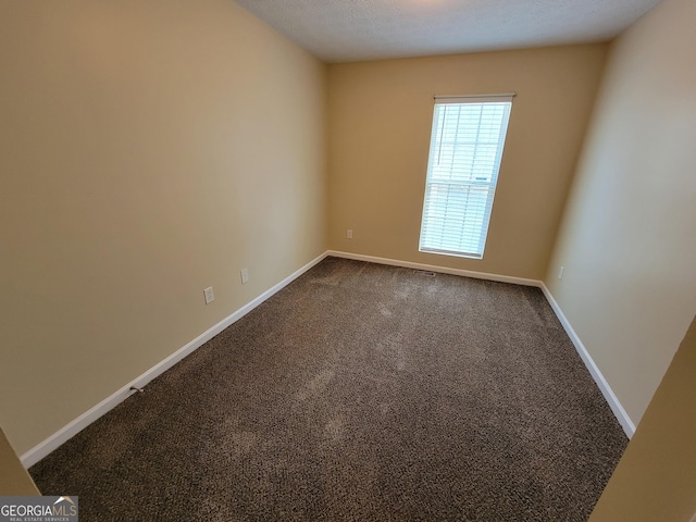 unfurnished room with baseboards and dark carpet