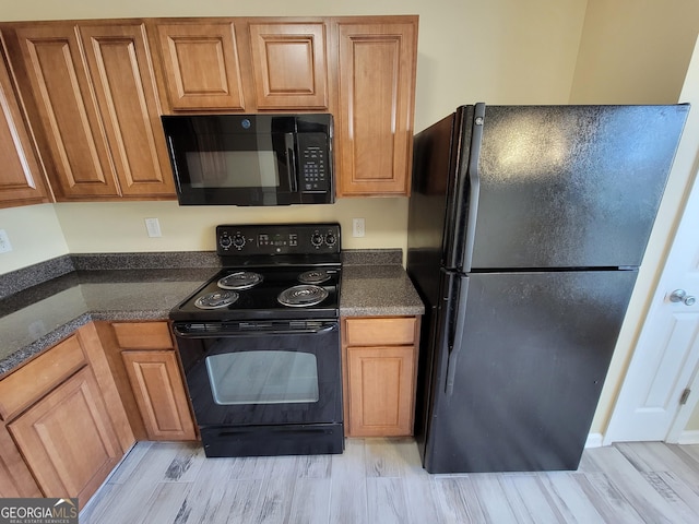 kitchen with dark stone counters, black appliances, light wood-type flooring, and brown cabinets