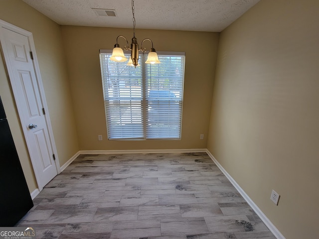 unfurnished dining area featuring visible vents, a textured ceiling, baseboards, and an inviting chandelier