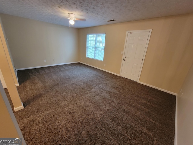 empty room with a textured ceiling, a ceiling fan, visible vents, baseboards, and dark carpet