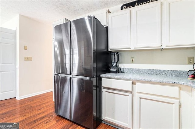 kitchen featuring a textured ceiling, dark wood-style flooring, white cabinetry, baseboards, and freestanding refrigerator