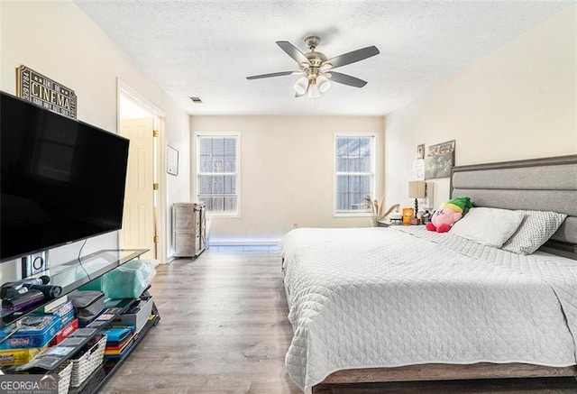 bedroom featuring baseboards, visible vents, ceiling fan, wood finished floors, and a textured ceiling